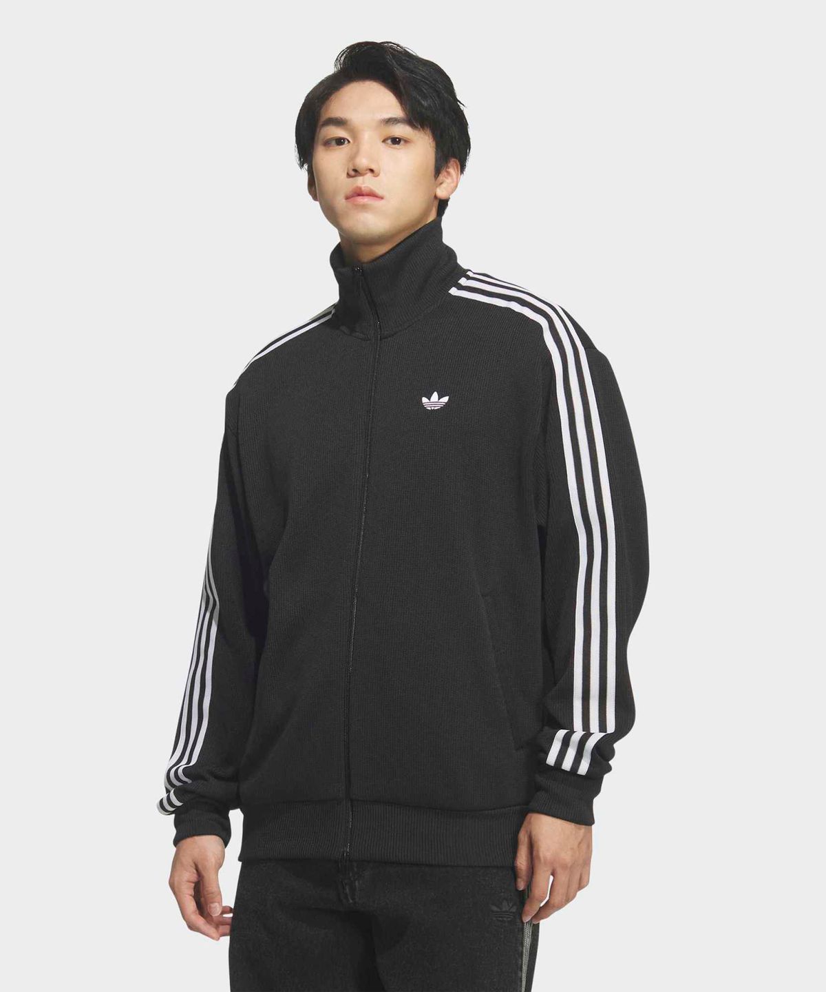 트랙탑 가슴 부분의 흰색 트레포일 로고 자수와 지퍼 디테일을 근접해서 촬영한 사진
