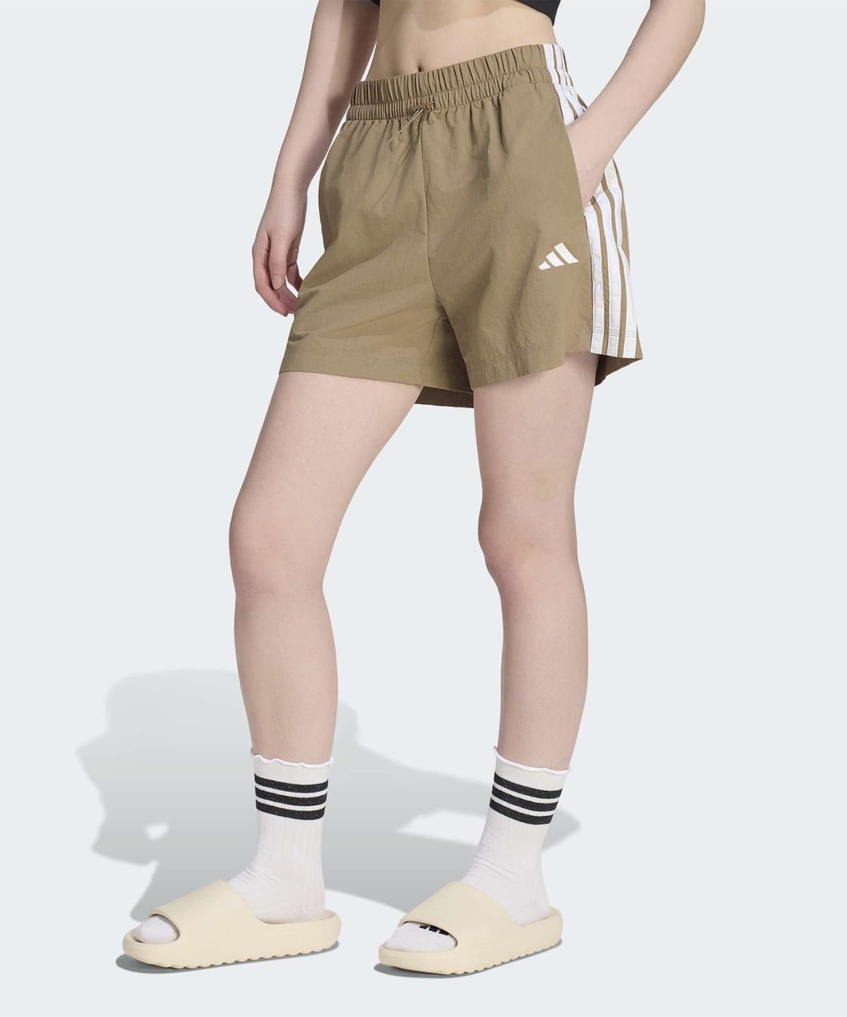 카키색 아디다스 우븐 숏 팬츠가 침대 위에 깔끔하게 놓여 있는 모습